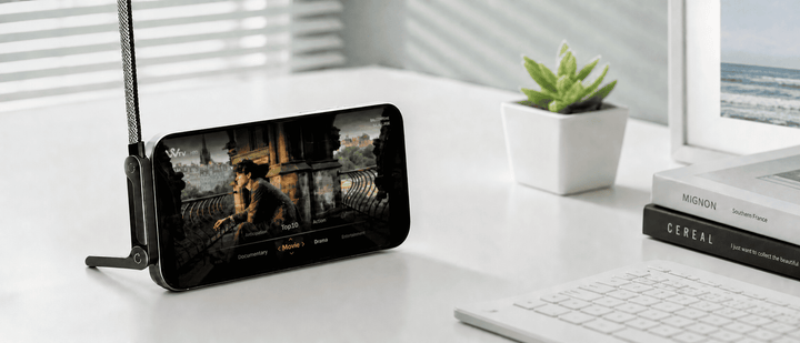 A smartphone on a desk mount displaying a movie streaming app, set on a bright, minimalist workspace.